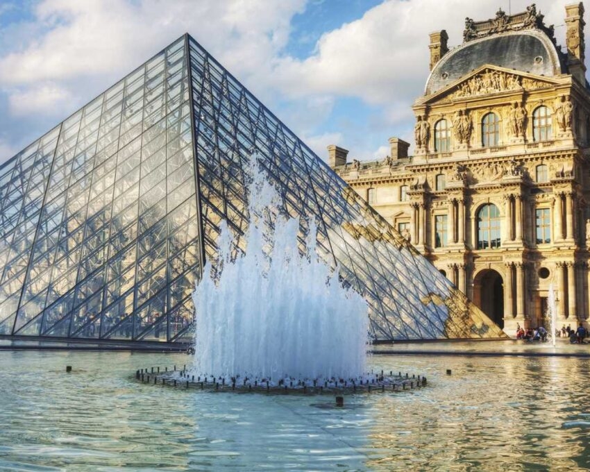 The glass Louvre Pyramid behind a splashing water fountain in Paris.