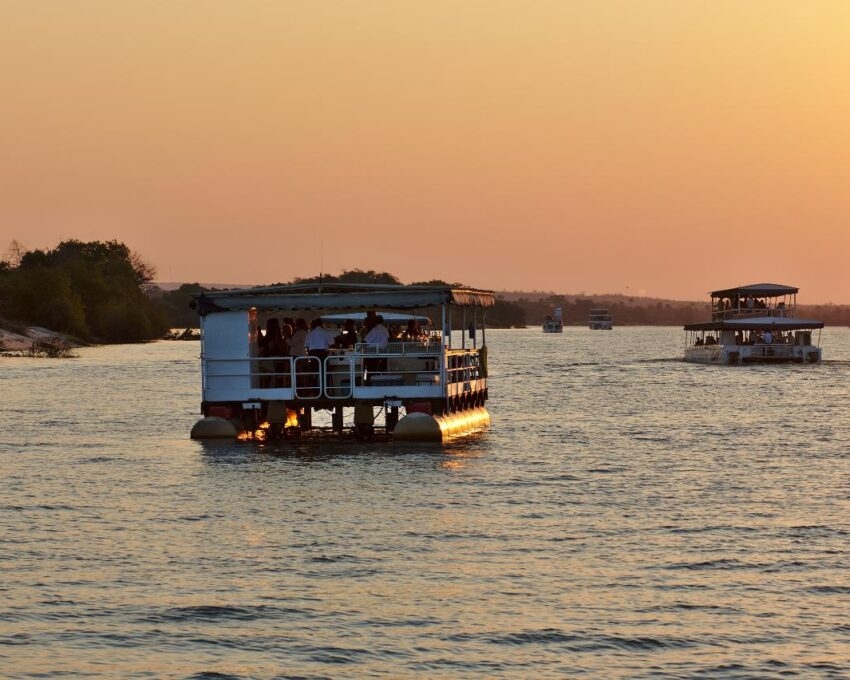 Large tourist boats on a river at sunset with orange light reflecting on the water and a clear sky.