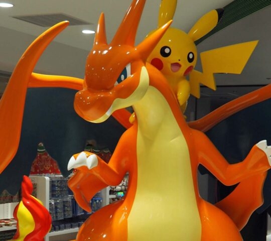 A large, glossy orange statue of Charizard with a smaller, yellow Pikachu statue mounted behind its head, in a retail store.