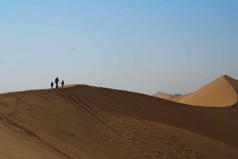 Silhouette of three figures walking on the crest of a high sand dune in the desert.