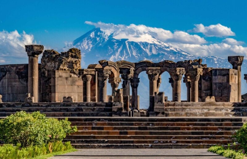 Ancient stone arches and columns with a mountain backdrop on luxury Central Asia trips.
