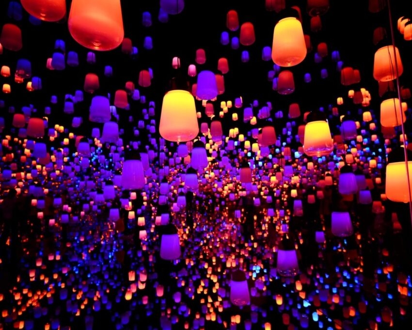 Hundreds of illuminated orange, red, and blue lanterns hanging in a dark space, creating an immersive, infinite reflection effect.