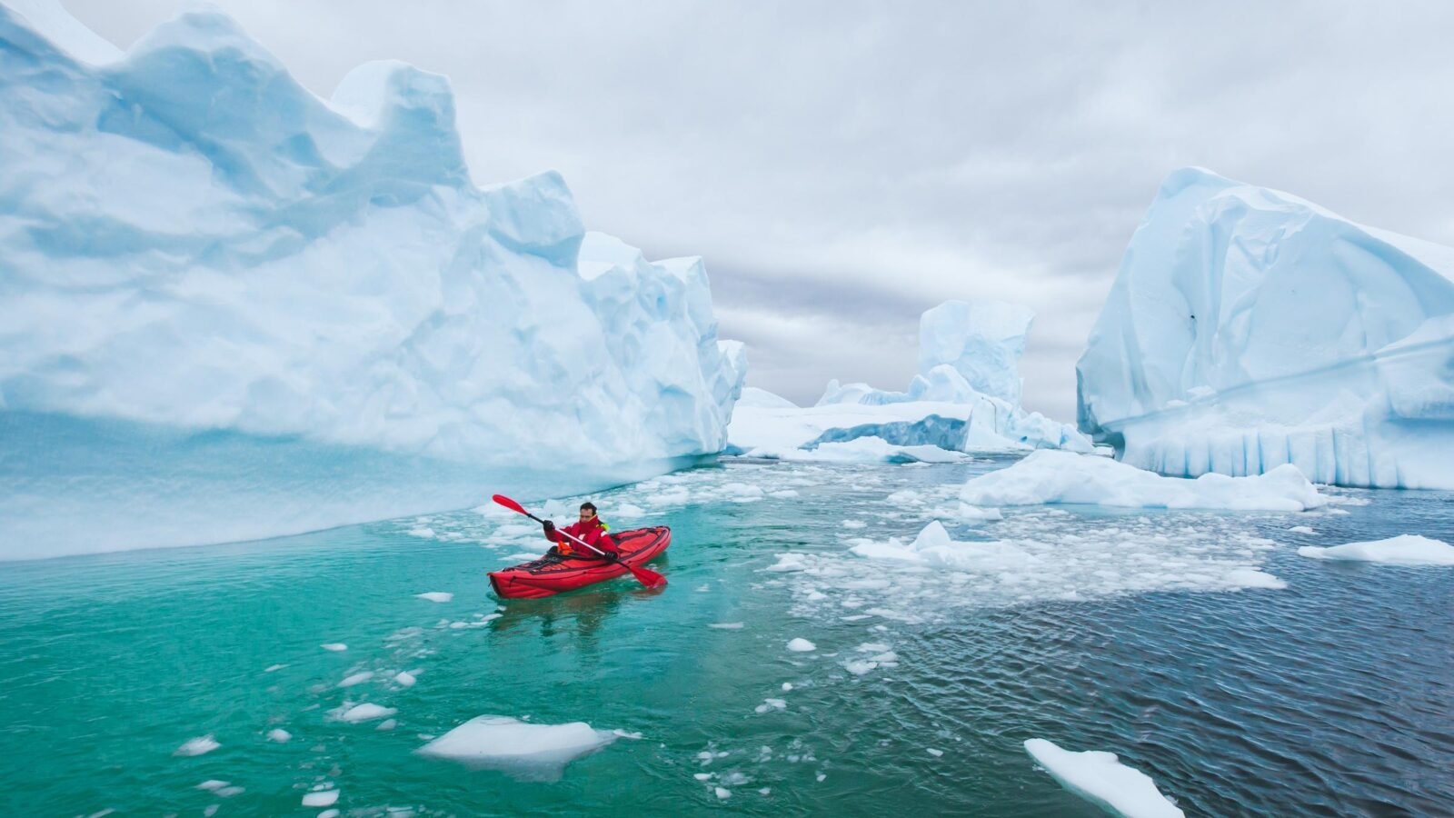 man paddling on kayak between ice in Antractica in Iceberg Graveyard, extreme winter kayaking, polar adventure near Pleneau island