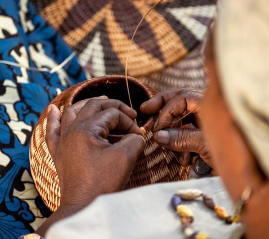 A woman weaves a basket by hand using traditional methods