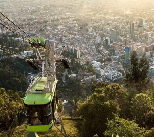 Green funicular carriage ascending on a wire to Monserrat in Bogota with skyscrapers in the background