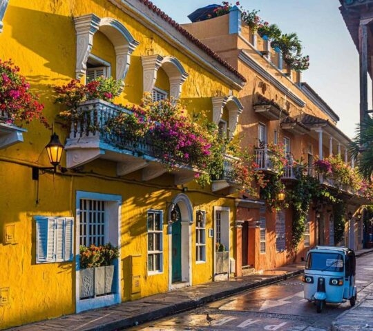 A beautiful street with bright yellow Colonial-style buildings and a motorised tuk tuk on the road in Cartagena, Colombia