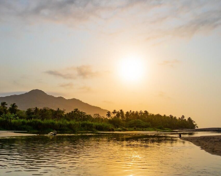 A wide river flows through the tropical rainforest of South America at a beautiful sunset where people bathe and enjoy life, Colombia Palomino