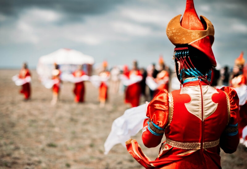 A person in a red and gold traditional costume in an open field during luxury Mongolia vacations.