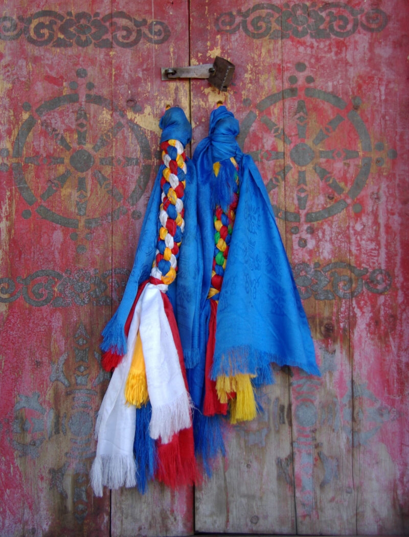 Braided silk scarves draped over a red wooden door, reflecting the traditions of luxury Mongolia holidays.