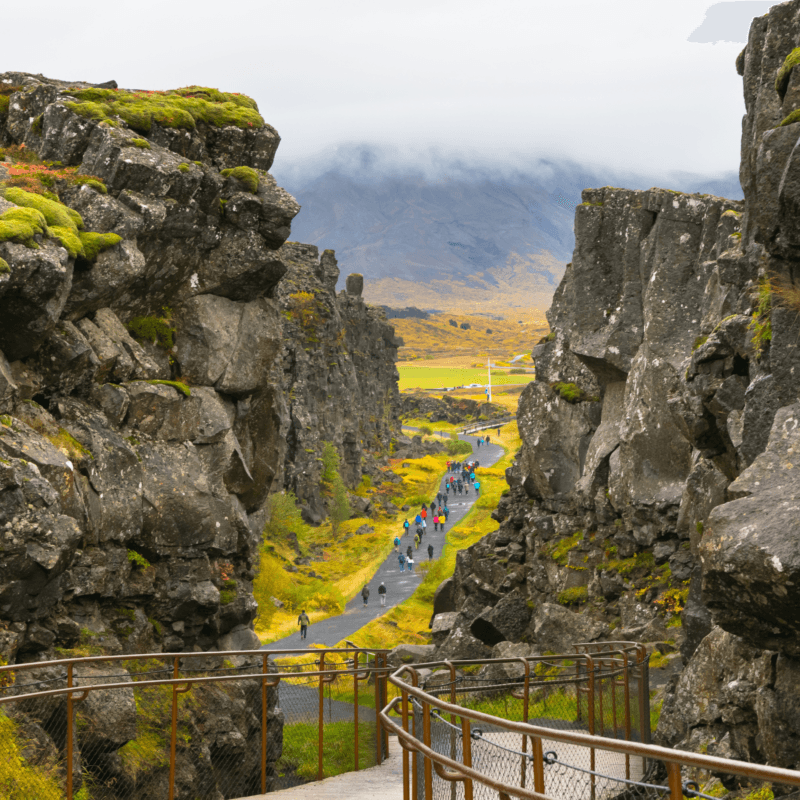 A group of people walking on a paved trail between towering rock formations under a cloudy sky during luxury Golden Circle tours.