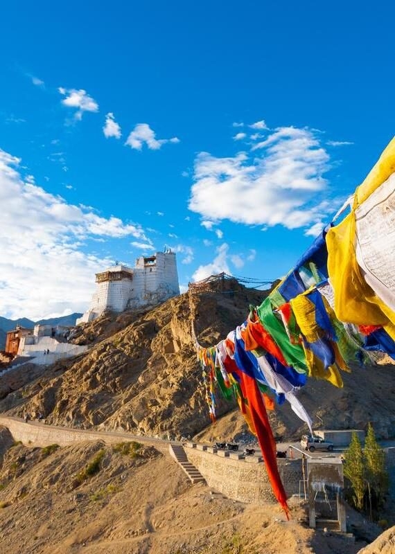 Colorful prayer flags in the foreground with a white mountain monastery and blue sky in the background.