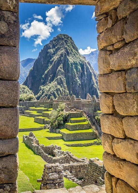 A view of Machu Picchu's stone structures and Huayna Picchu mountain framed through a stone window.