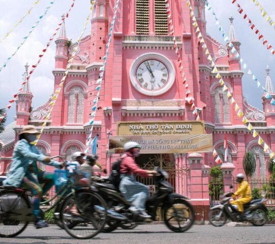 Scooters going past a pink catholic church in Ho Chi Minh City, Vietnam