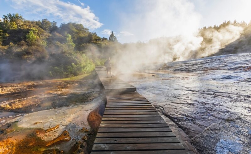 Tourist on a wooden boardwalk surrounded by steam from geothermal activity, Lake Taupo, New Zealand