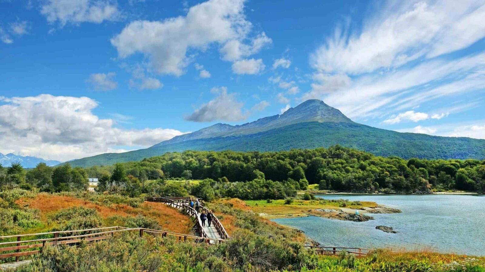 Panoramic view of Tierra del Fuego National Park, showing a volcano surrounded by green vegetation and water, against a blue sky.