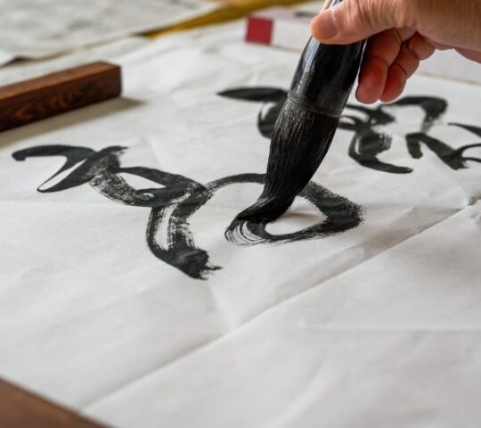 Hand practicing calligraphy with a brush on white paper.
