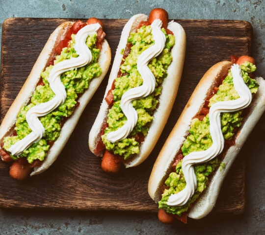 Chilean Completo Italiano. Hot dog sandwiches with tomato, avocado and mayonnaise on wooden board. Top view.