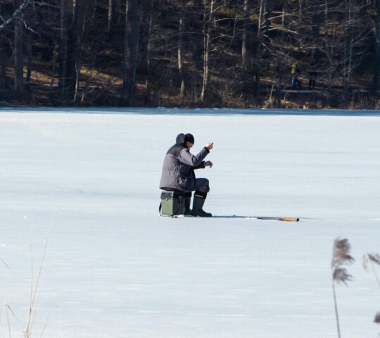 Fisherman fishing on a frozen lake in the early spring with fishing pole, ice auger and equipment for fishing