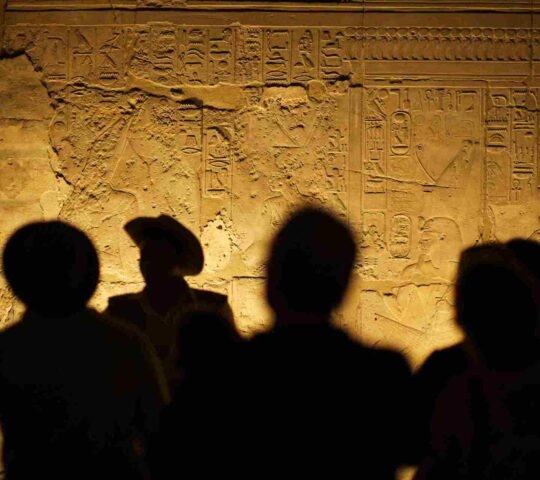 Group of unrecognizable tourist archeologists standing in silhouette in front of ancient Egyptian hieroglyphs