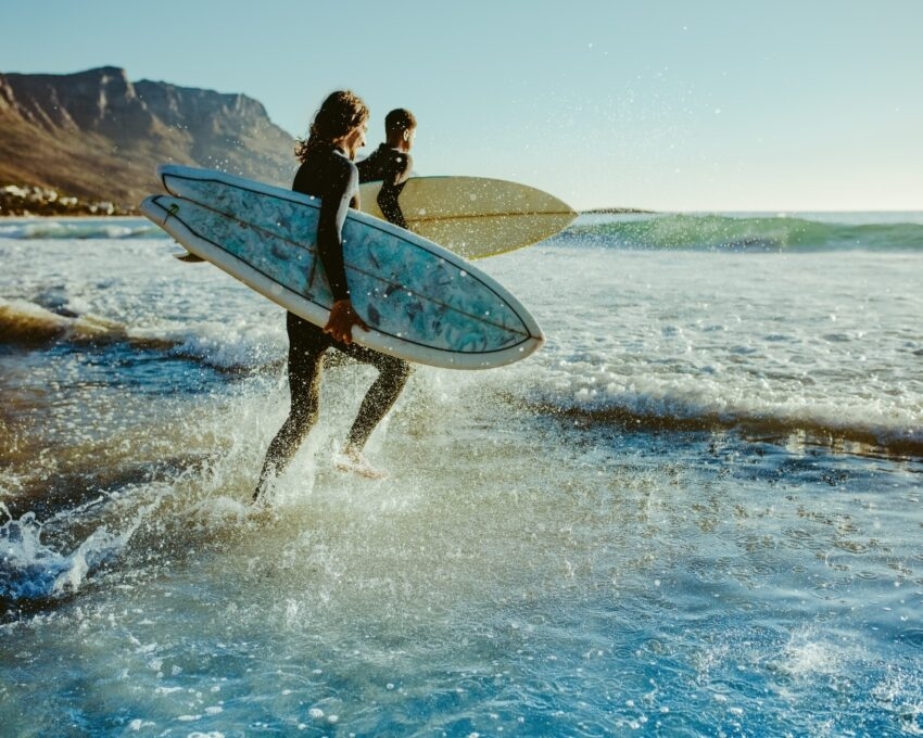 Two male surfers going for surfing in the sea. Two men carrying surfboards running in to the sea for surfing.
