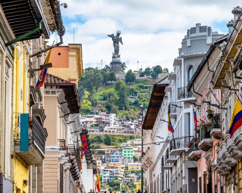 A colorful street with flags leading to a hilltop statue under a cloudy sky.