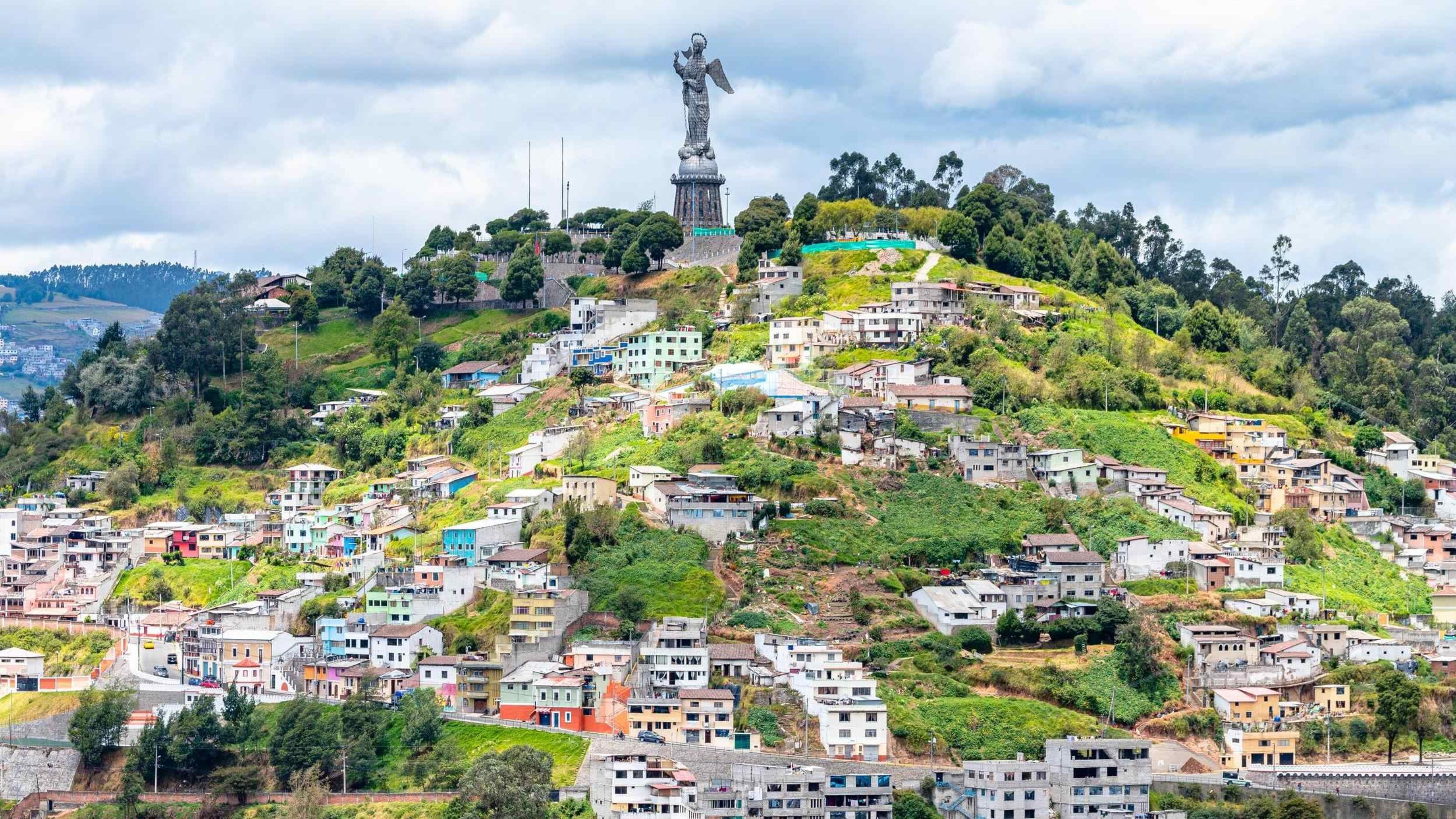 Hillside cityscape with colorful houses and a large statue on top of the hill.