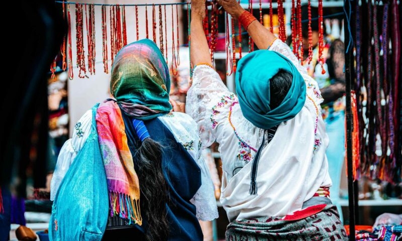 Two people examining jewelry at a colorful market stall.