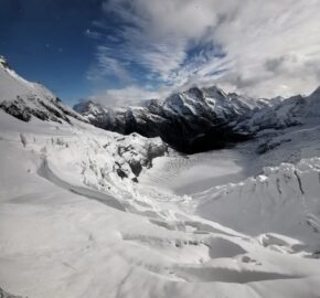 Snow-covered mountain landscape with a glacier and cloudy blue sky.