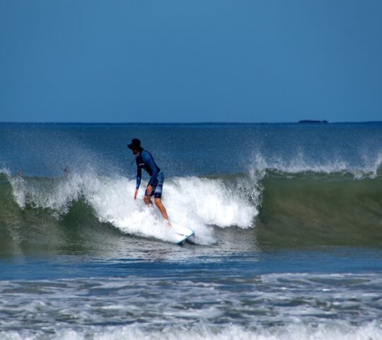 A surfer riding a wave in the ocean under a clear blue sky.