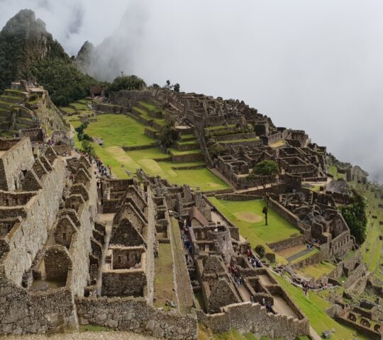 Machu Picchu ruins with tourists and misty mountains in the background.