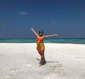 Person with arms outstretched on a sandy beach against a clear blue sky.
