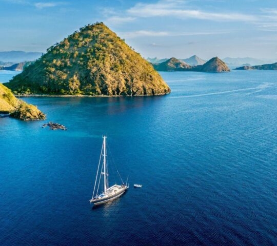 Sailboat with island under blue sky Aerial view of sailboat with island under blue sky in Labuan Bajo near Bali Island, Indonesia
