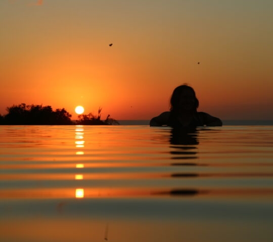 Person in water with reflection of a sunset over the horizon.