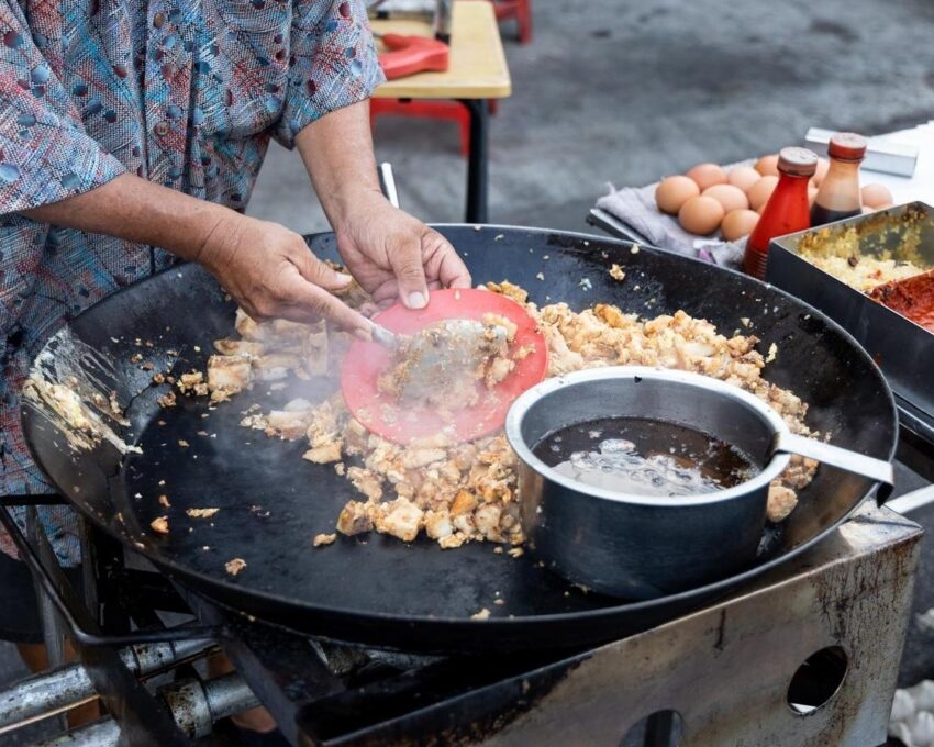 Person cooking food in a large wok on an outdoor stove.