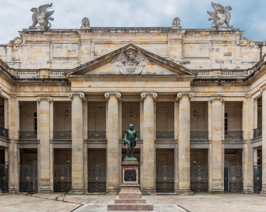 Colonial building facade with statue in front under cloudy sky.