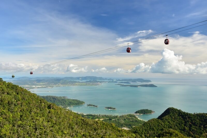 Cable cars over a tropical coast with islands and blue sea under a cloudy sky.