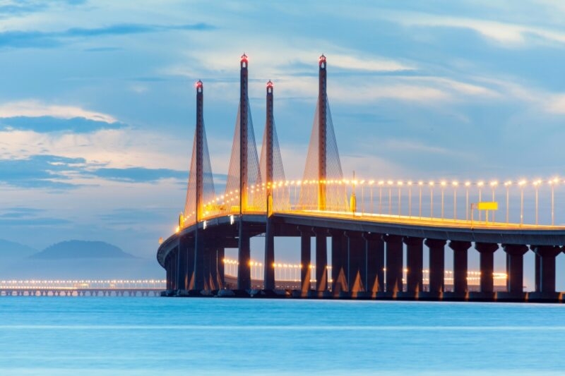 A long bridge with tall pillars and lights against a twilight sky.