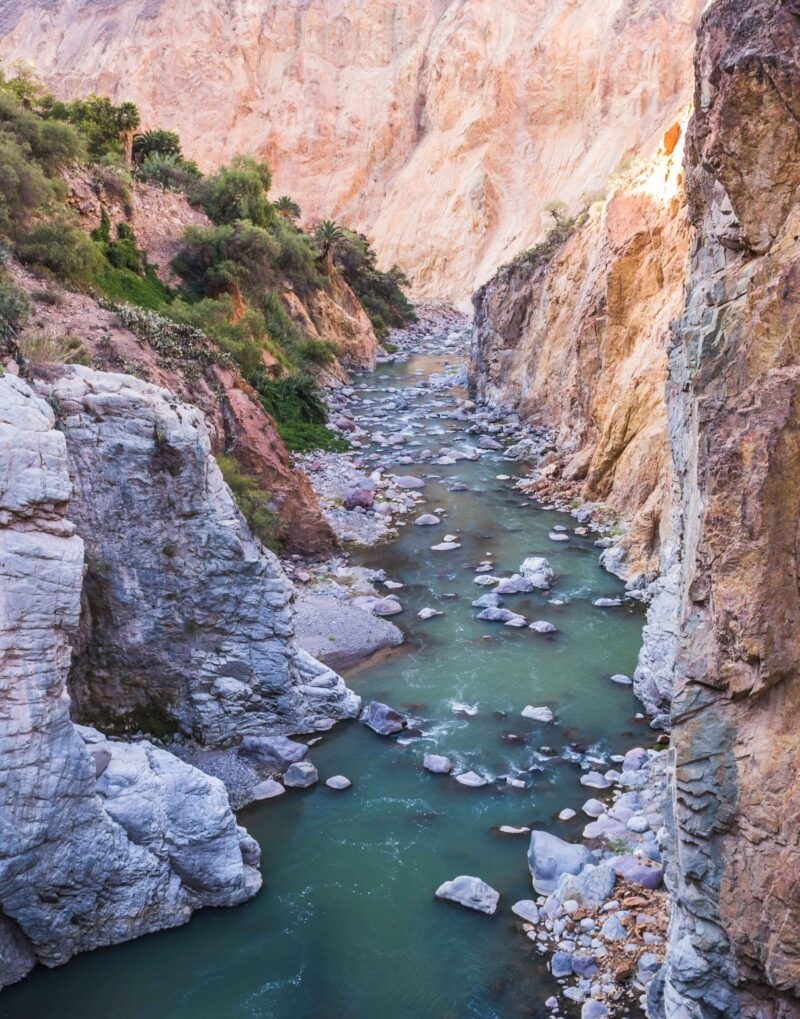 A serene river flowing through a rugged canyon with steep, colorful cliffs and scattered rocks.