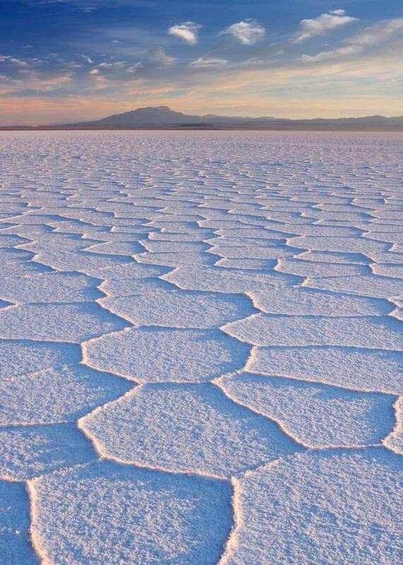 Hexagonal salt flats with a mountain in the distance under a twilight sky.