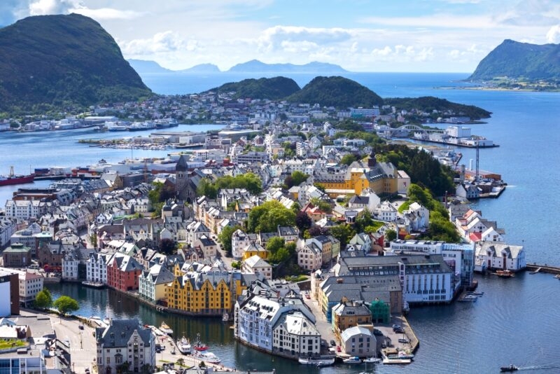 Aerial view of a colorful coastal town with buildings near the water's edge, backed by mountains.