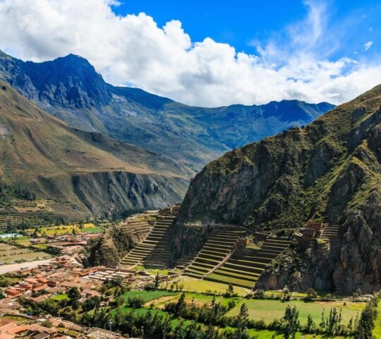 Mountainous landscape with terraced fields, a small village, and sunny blue skies.