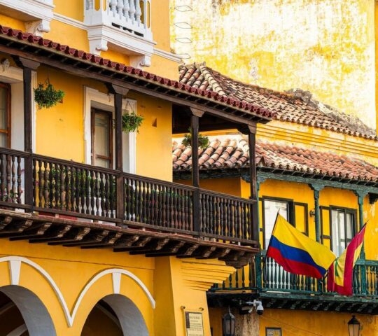 Yellow colonial building facade with balcony and flags in Cartagena, Colombia.