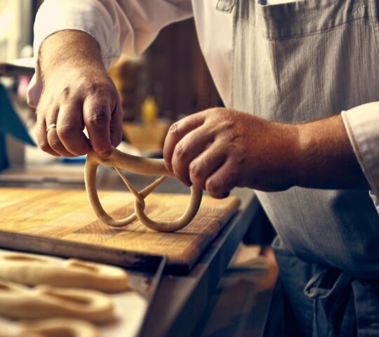 Chef in an apron shaping dough on a wooden board.