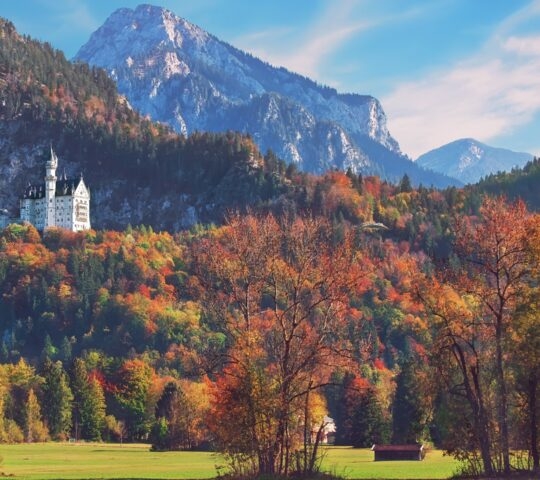 A fairytale castle nestled among forested mountains during autumn foliage.