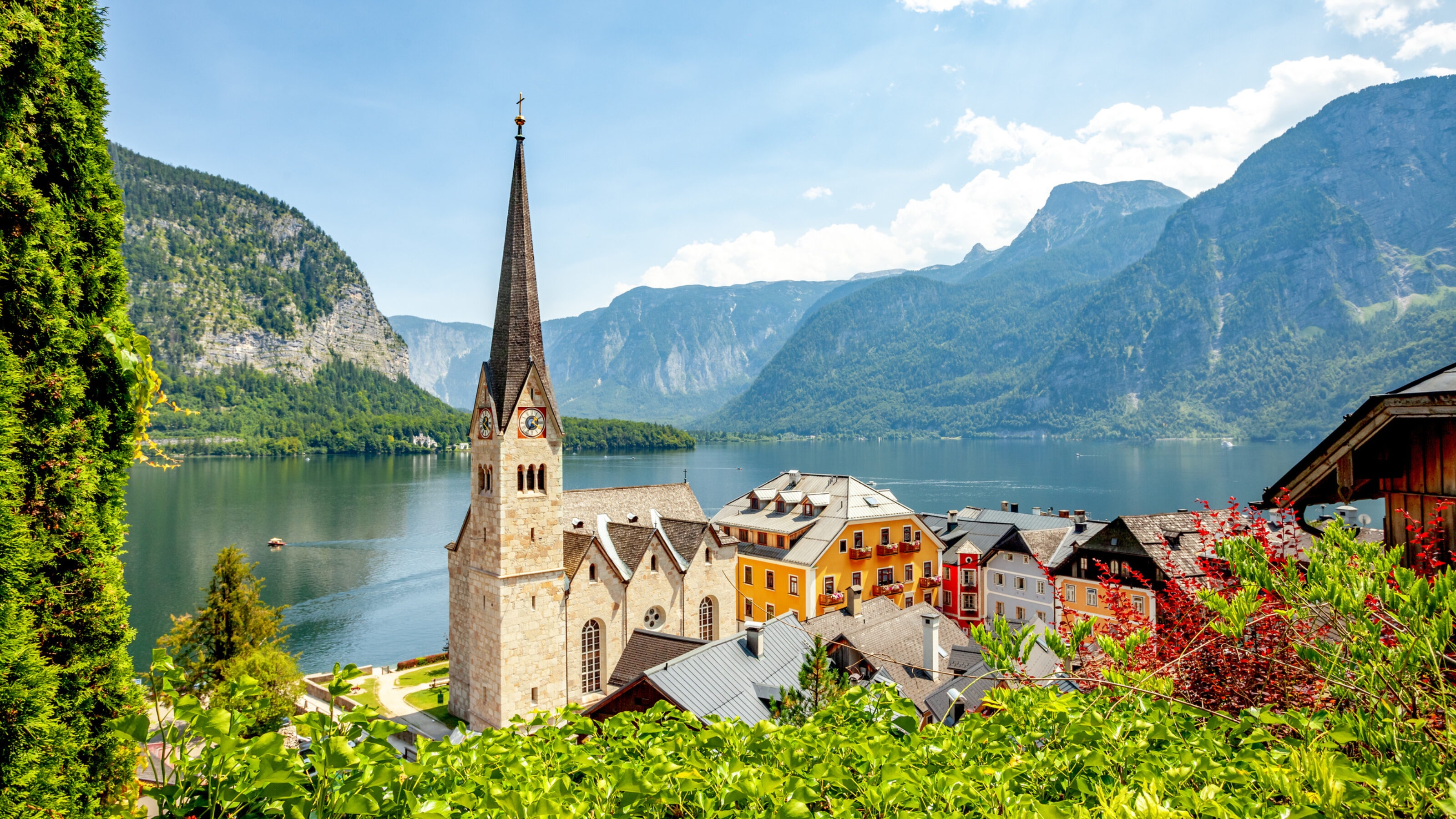A picturesque village with colorful houses and a church by a lake, against a backdrop of mountains.