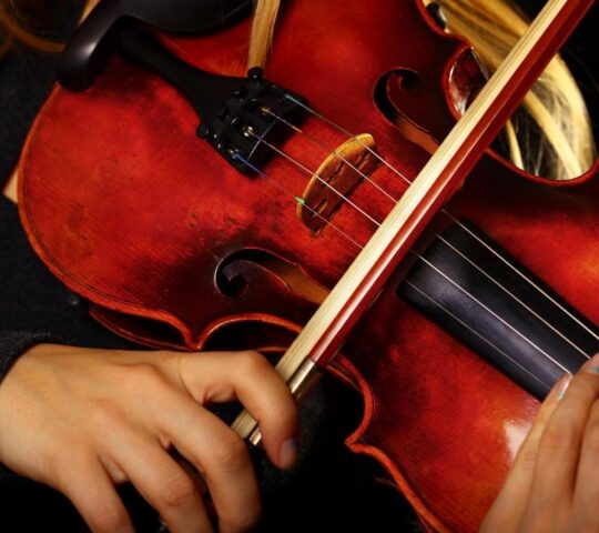 Close-up of hands playing a violin with a bow.