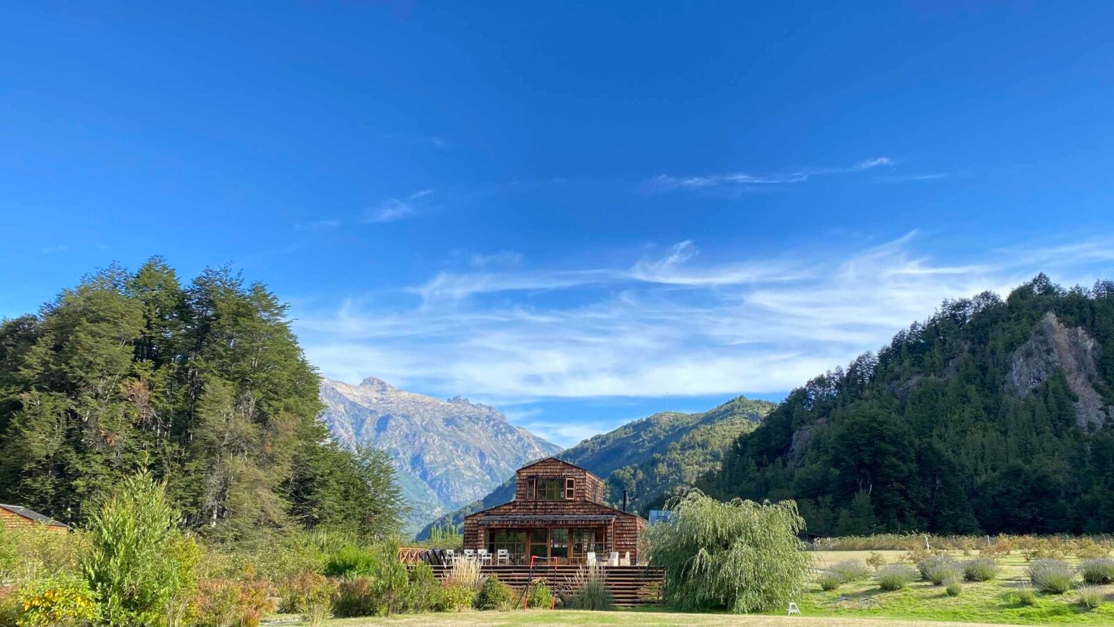 Wooden cabin in a mountain valley with clear blue skies and greenery.