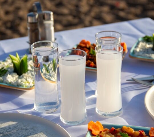 Outdoor dining setup with glasses of water and milk, and plates of fresh food.