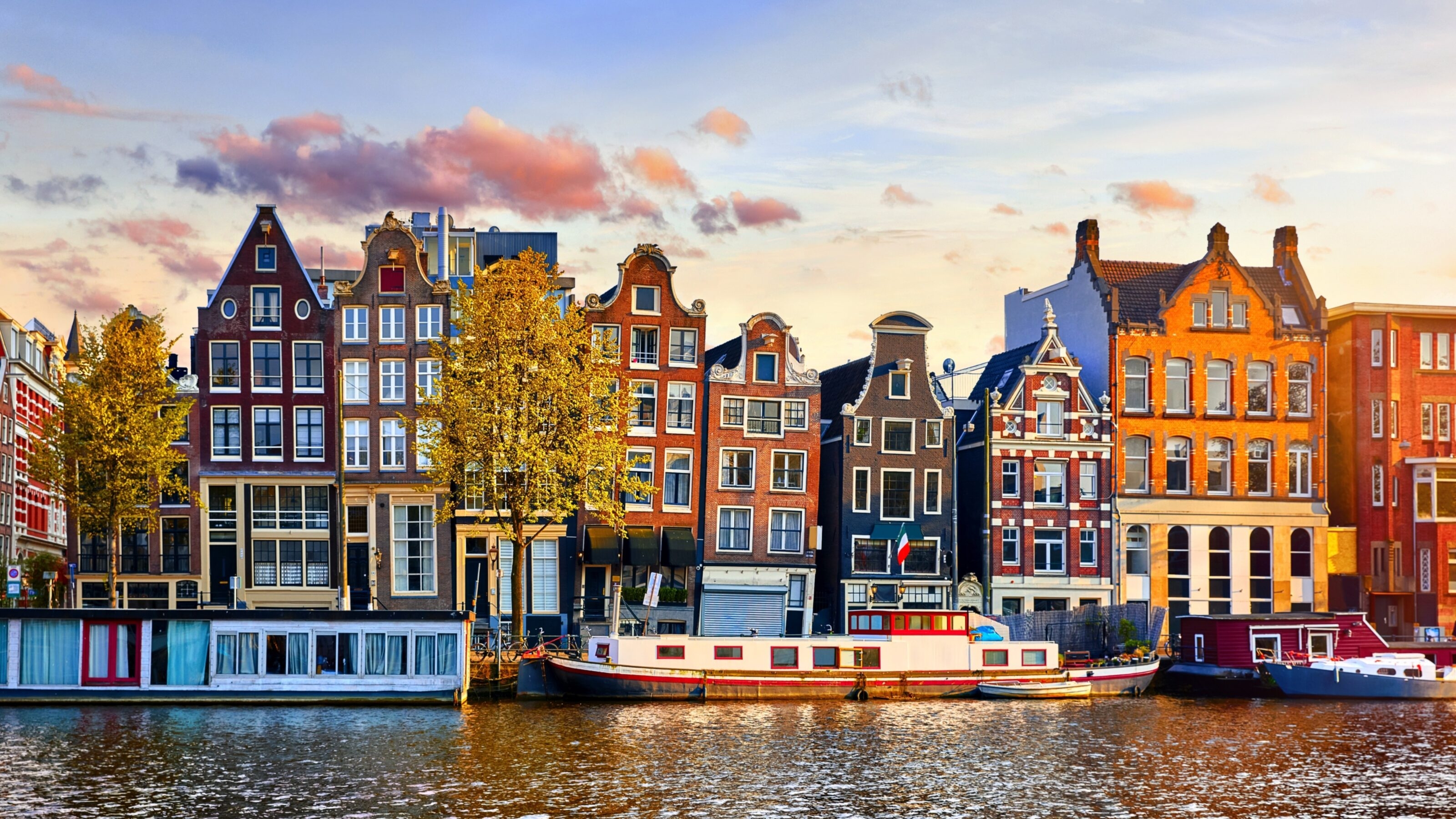 Colourful Dutch houses by a canal at sunset with a houseboat in Amsterdam.
