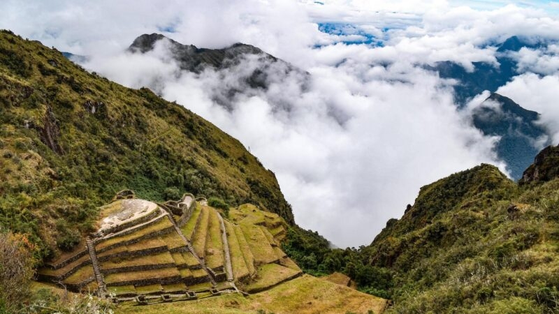 Stone terraces of an Inca ruin on a lush mountainside surrounded by clouds during luxury Inca Trail tours.